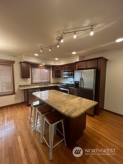 kitchen with a kitchen island, a breakfast bar area, rail lighting, stainless steel appliances, and light hardwood / wood-style flooring