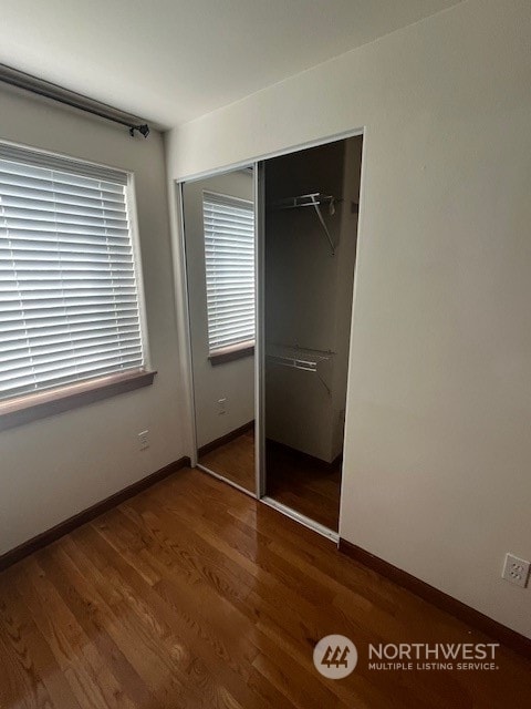 unfurnished bedroom with a closet, multiple windows, and dark hardwood / wood-style floors