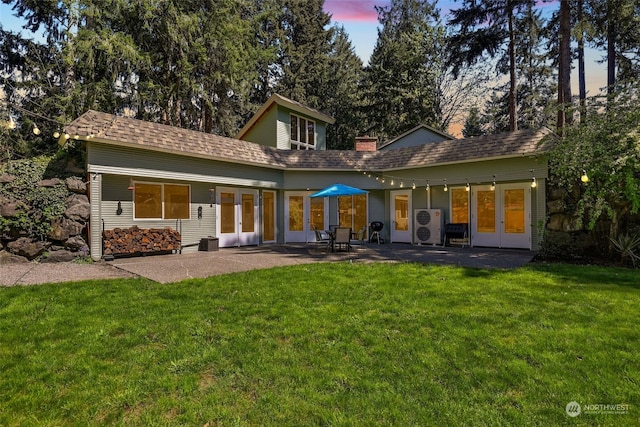 back house at dusk featuring a patio area, a yard, and french doors