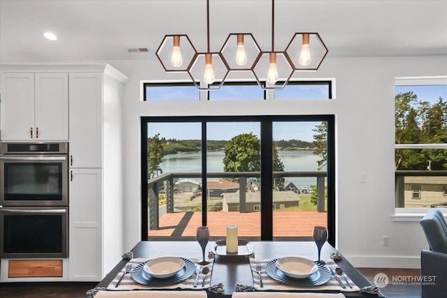 dining room featuring dark wood-type flooring, a water view, a healthy amount of sunlight, and an inviting chandelier