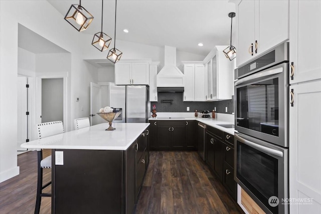 kitchen with appliances with stainless steel finishes, decorative light fixtures, a kitchen island, a kitchen bar, and white cabinetry