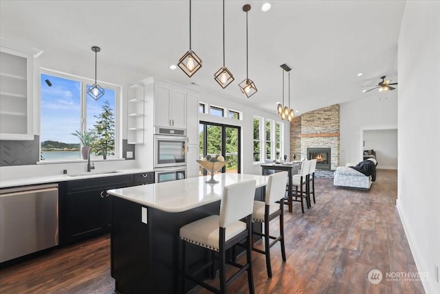 kitchen with a kitchen breakfast bar, stainless steel appliances, ceiling fan, pendant lighting, and a fireplace