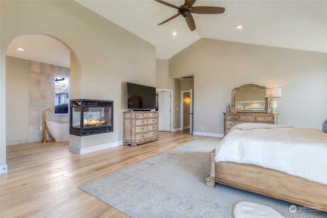 bedroom with ceiling fan, a multi sided fireplace, high vaulted ceiling, and light hardwood / wood-style flooring