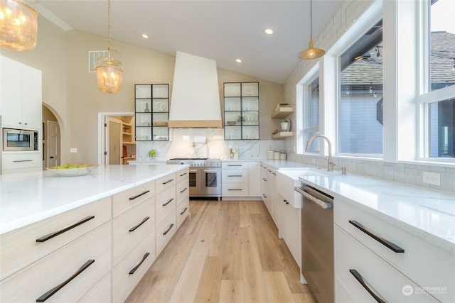 kitchen with premium range hood, white cabinetry, stainless steel appliances, tasteful backsplash, and decorative light fixtures