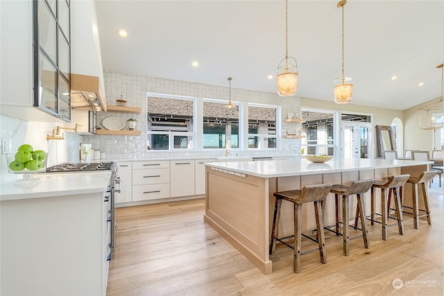 kitchen featuring high end stainless steel range, white cabinetry, a center island, hanging light fixtures, and light hardwood / wood-style floors