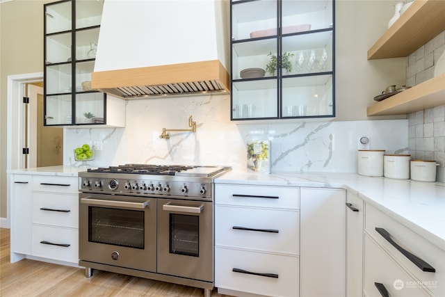 kitchen with white cabinetry, light stone counters, tasteful backsplash, custom exhaust hood, and range with two ovens