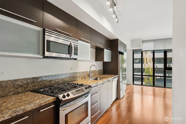 kitchen with appliances with stainless steel finishes, light wood-type flooring, dark stone counters, and sink