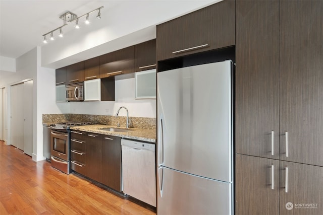 kitchen with appliances with stainless steel finishes, light stone counters, dark brown cabinets, and sink