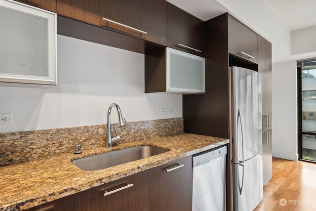 kitchen with sink, stainless steel appliances, light stone counters, dark brown cabinets, and light wood-type flooring