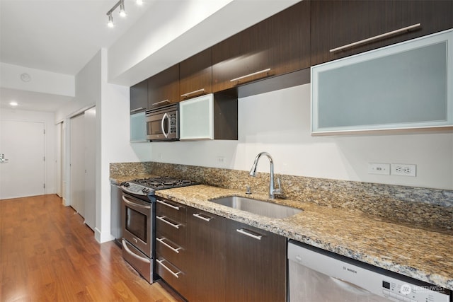 kitchen featuring sink, light stone countertops, appliances with stainless steel finishes, dark brown cabinets, and light hardwood / wood-style floors