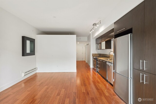 kitchen with appliances with stainless steel finishes, dark brown cabinets, a baseboard heating unit, sink, and light hardwood / wood-style flooring