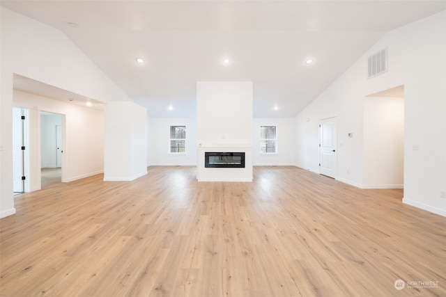 unfurnished living room featuring light wood finished floors, visible vents, high vaulted ceiling, and a glass covered fireplace