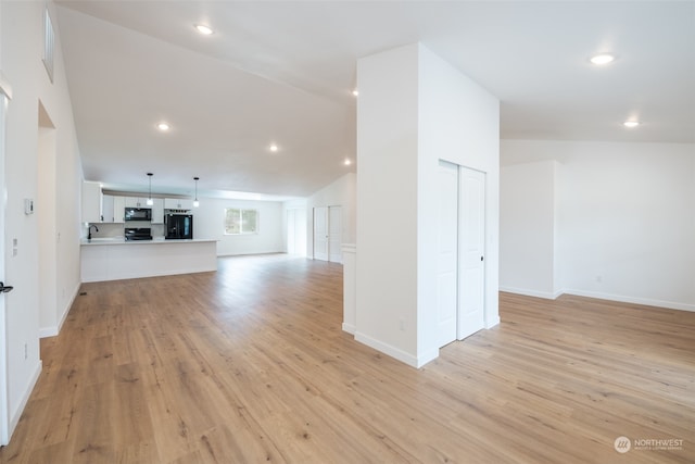 unfurnished living room with sink, high vaulted ceiling, and light wood-type flooring