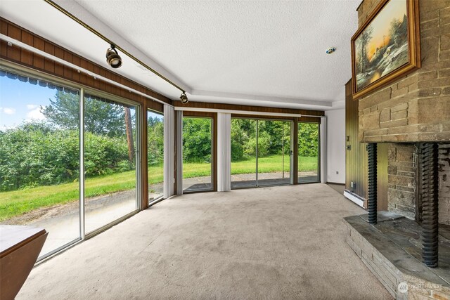 unfurnished living room featuring carpet flooring, a stone fireplace, a textured ceiling, and a baseboard heating unit