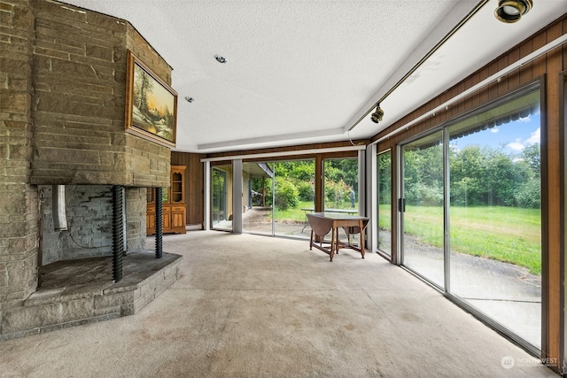 unfurnished living room with a stone fireplace, wood walls, carpet, and a textured ceiling