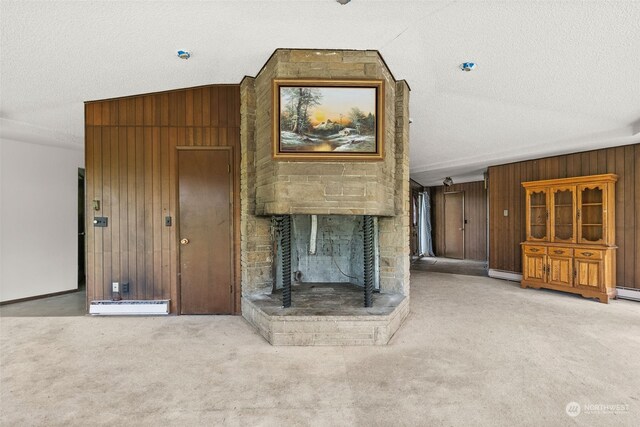 unfurnished living room featuring a textured ceiling, wood walls, a fireplace, and light carpet