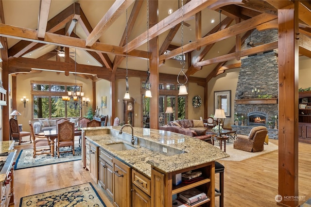 kitchen with light stone countertops, sink, decorative light fixtures, high vaulted ceiling, and light hardwood / wood-style floors