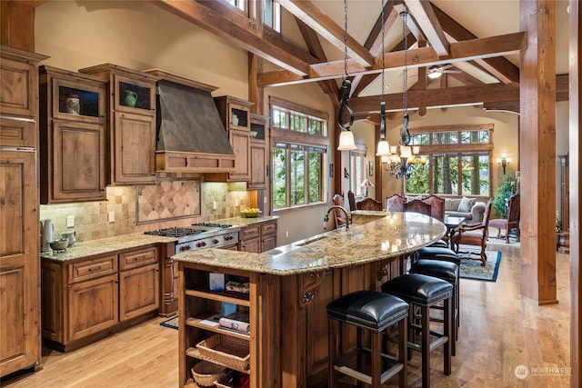 kitchen with plenty of natural light, light hardwood / wood-style floors, custom range hood, and a large island with sink