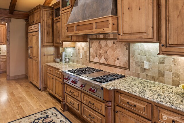 kitchen with light wood-type flooring, light stone counters, custom exhaust hood, stainless steel gas cooktop, and beamed ceiling