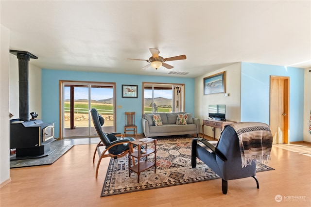 living room featuring a wood stove, light hardwood / wood-style flooring, and ceiling fan