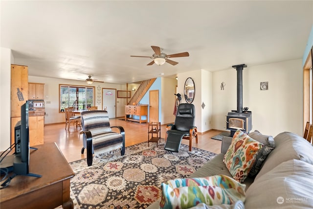 living room with light hardwood / wood-style flooring, a wood stove, and ceiling fan