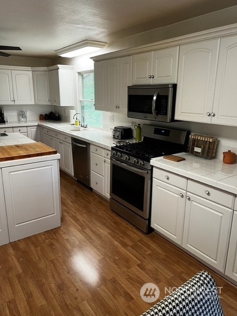 kitchen with hardwood / wood-style flooring, appliances with stainless steel finishes, white cabinetry, and sink