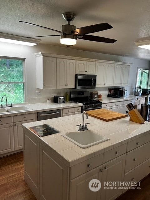 kitchen featuring an island with sink, ceiling fan, tile countertops, and range with gas stovetop