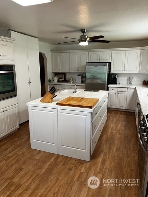 kitchen featuring ceiling fan, white cabinets, hardwood / wood-style floors, stainless steel appliances, and a kitchen island with sink