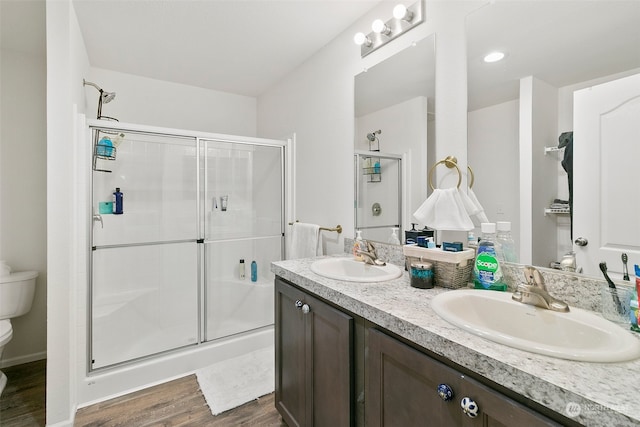 bathroom with vanity with extensive cabinet space, wood-type flooring, a shower with door, dual sinks, and toilet