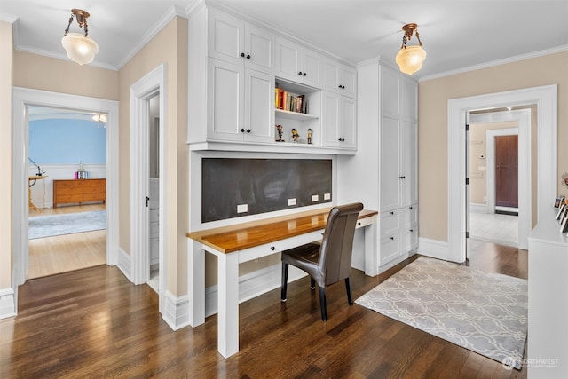 home office with ornamental molding, built in desk, and dark hardwood / wood-style flooring