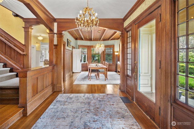 foyer featuring ornamental molding, hardwood / wood-style flooring, a chandelier, and decorative columns