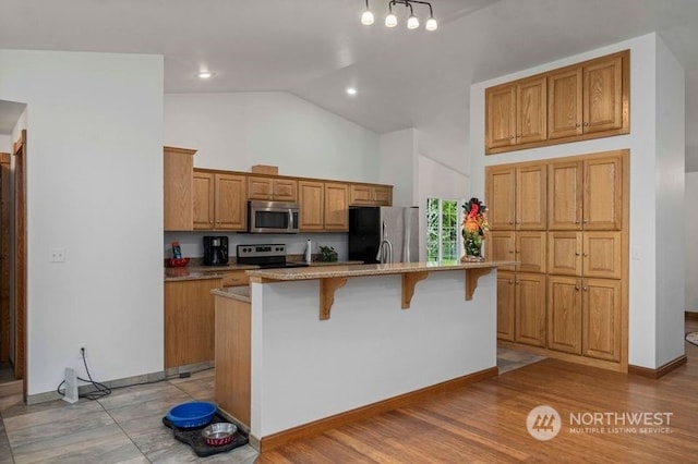 kitchen with a breakfast bar area, a center island with sink, light wood-style flooring, stainless steel appliances, and brown cabinets