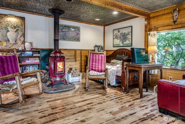 sitting room with wood-type flooring, ornamental molding, a wood stove, and wooden walls