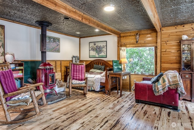 living area with beam ceiling, wooden walls, wood-type flooring, and a wood stove