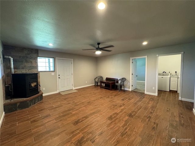 unfurnished living room with ceiling fan, a wood stove, dark wood-type flooring, and washer and dryer