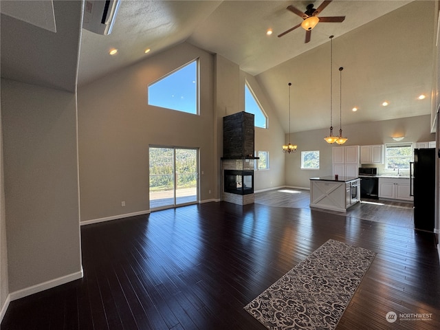 unfurnished living room with a multi sided fireplace, high vaulted ceiling, sink, ceiling fan with notable chandelier, and dark wood-type flooring