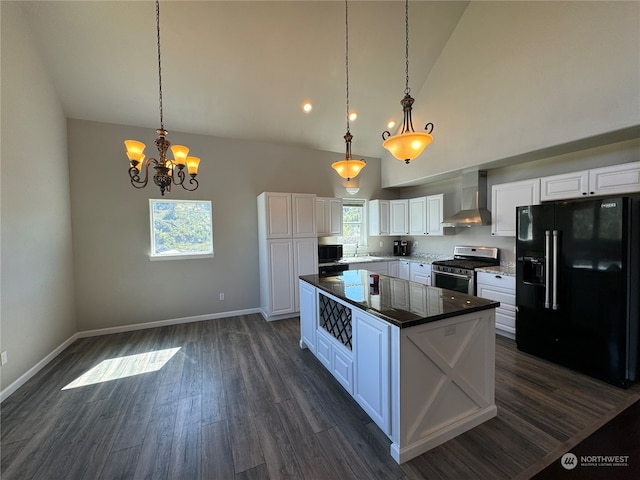 kitchen with wall chimney exhaust hood, a healthy amount of sunlight, hanging light fixtures, high end black fridge, and stainless steel gas stove