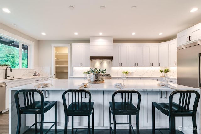 kitchen featuring light stone countertops, white cabinets, a spacious island, and sink