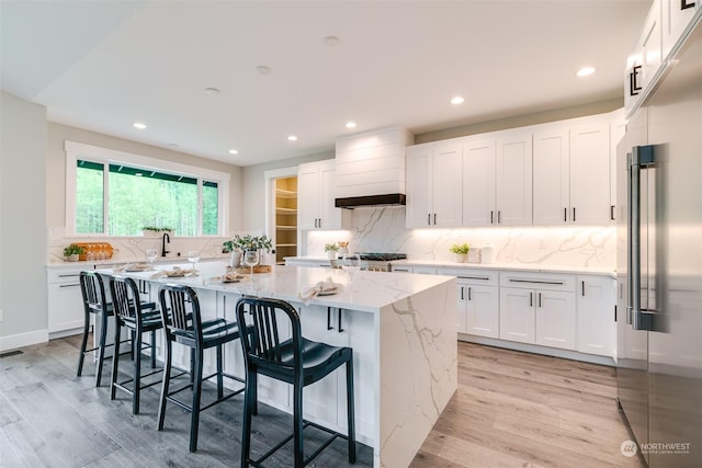 kitchen with backsplash, light stone counters, light hardwood / wood-style flooring, white cabinets, and a center island