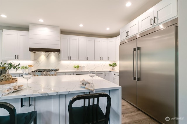 kitchen featuring light stone counters, light hardwood / wood-style flooring, backsplash, white cabinets, and appliances with stainless steel finishes