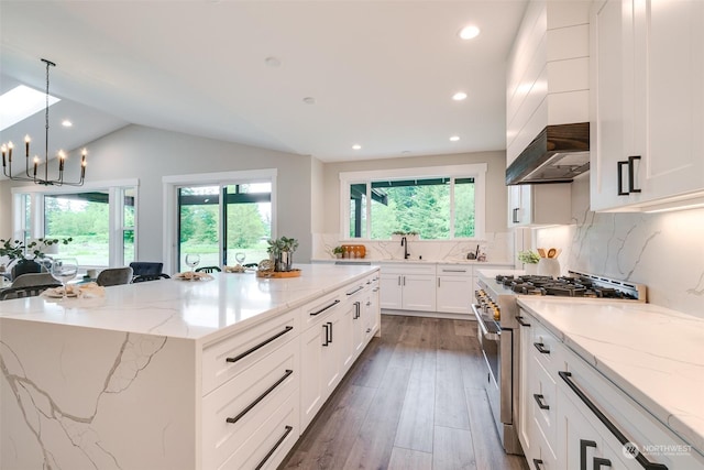 kitchen featuring lofted ceiling, a spacious island, white cabinetry, and high end stainless steel range oven