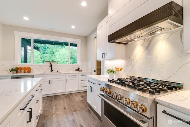 kitchen featuring backsplash, premium range hood, stainless steel range, sink, and white cabinetry