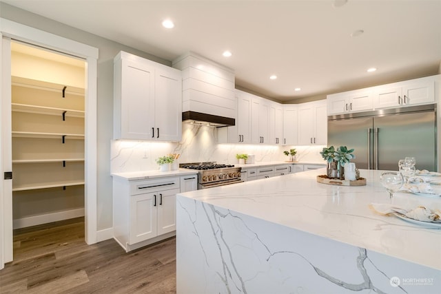 kitchen featuring white cabinetry, light stone countertops, backsplash, hardwood / wood-style floors, and high quality appliances