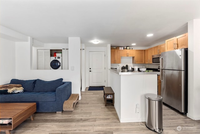 kitchen featuring light brown cabinets, light wood-type flooring, stainless steel appliances, and washer / dryer