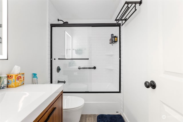 full bathroom with toilet, bath / shower combo with glass door, vanity, and hardwood / wood-style floors