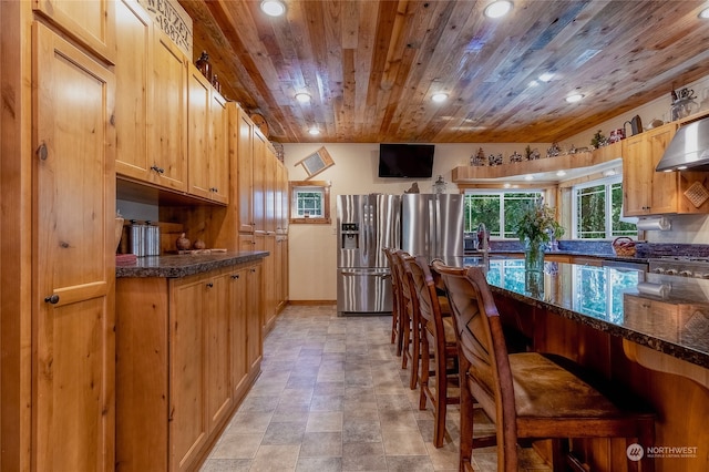 kitchen with wall chimney range hood, a kitchen bar, light tile floors, wood ceiling, and stainless steel fridge with ice dispenser