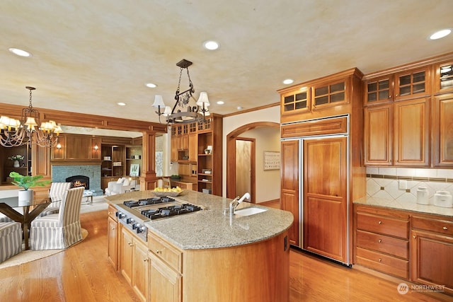 kitchen with pendant lighting, paneled built in refrigerator, light stone counters, an island with sink, and stainless steel gas stovetop