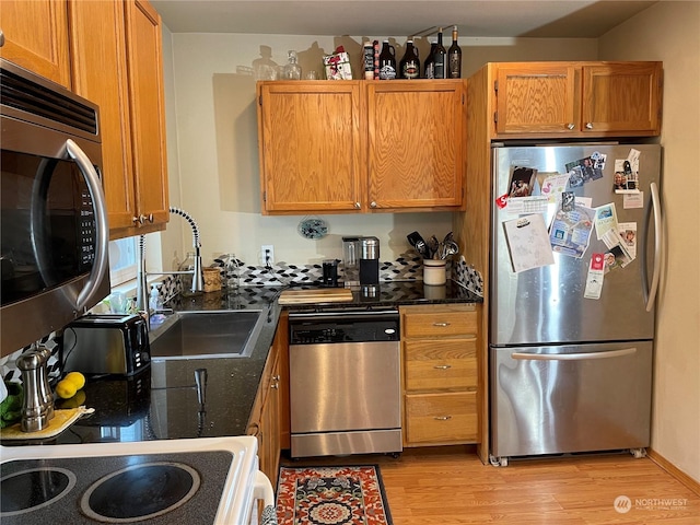 kitchen with stainless steel appliances, sink, light hardwood / wood-style flooring, and dark stone counters