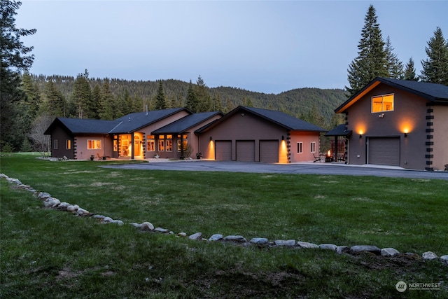 back house at dusk featuring a mountain view, a yard, and a garage