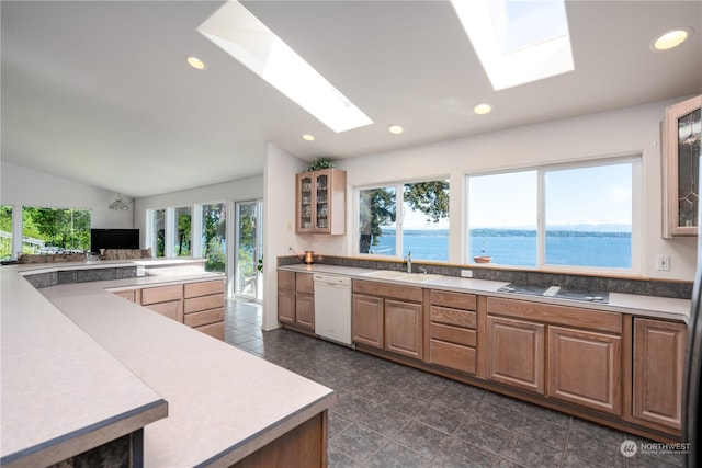 kitchen featuring a water view, white dishwasher, vaulted ceiling with skylight, and dark tile floors